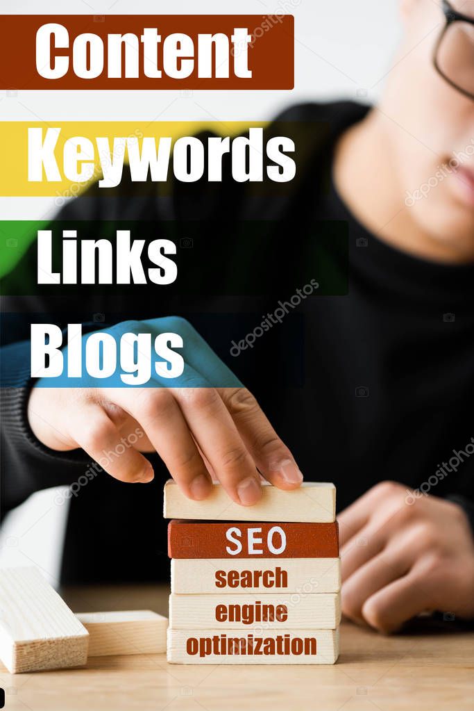 selective focus of seo manager stacking wooden rectangles with lettering near illustration with keywords, links, blogs words