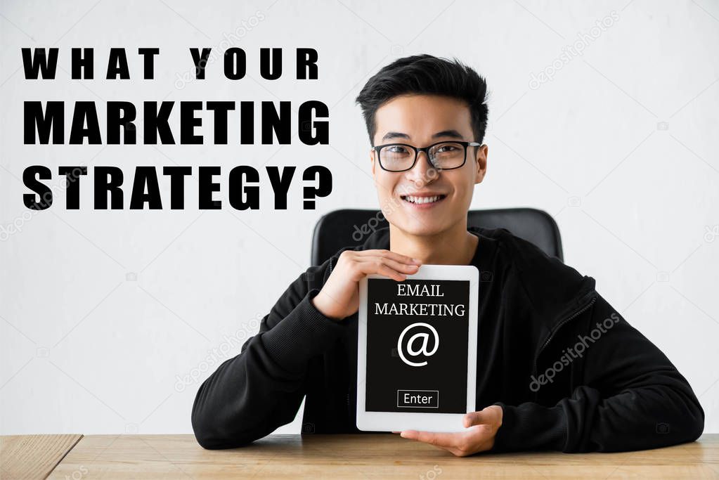 smiling asian seo manager holding digital tablet with e-mail marketing lettering and sitting near what your marketing strategy illustration