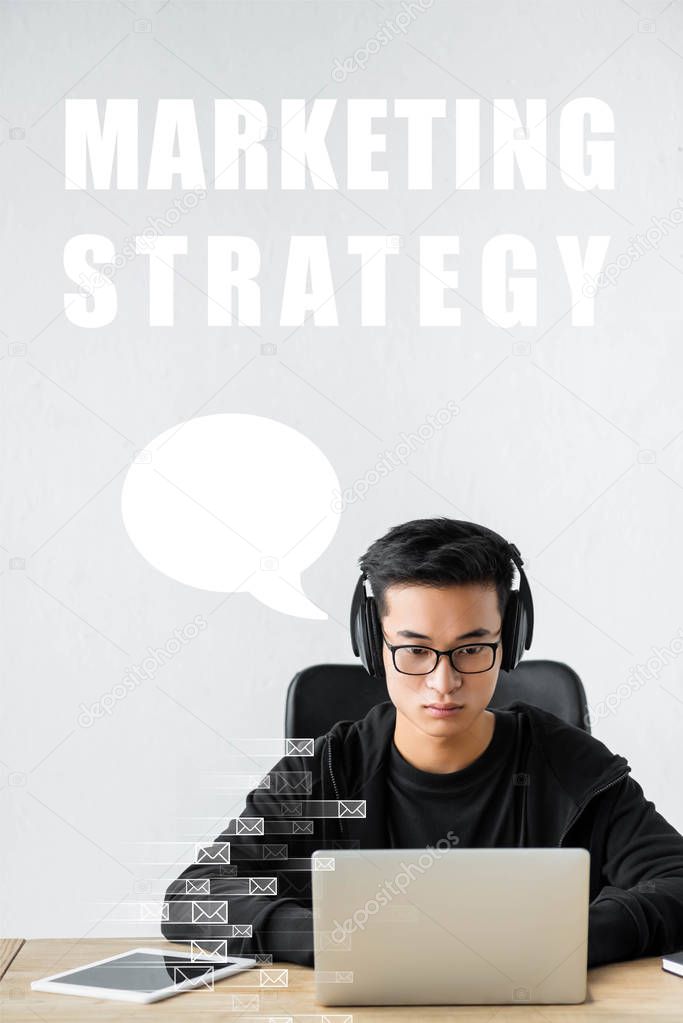 asian seo manager using laptop and sitting near marketing strategy illustration