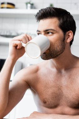 Yakışıklı, üstsüz adam sabahları mutfakta kahve içiyor.