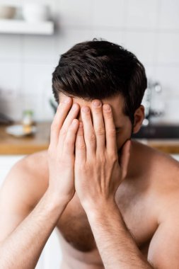 Mutfakta otururken suratını kapatan üzgün seksi adam.