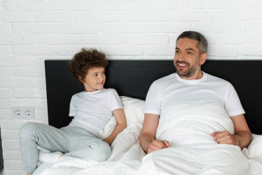 Kıvırcık çocuk yatak odasında sakallı babaya bakıyor. 
