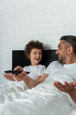 Mutlu çocuğun yanında uzaktan kumandayı tutan neşeli babanın seçici odağı.