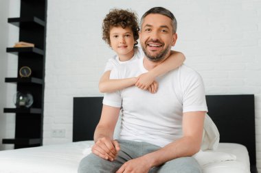 Kıvırcık oğlan, neşeli ve sakallı babaya sarılıyor. 