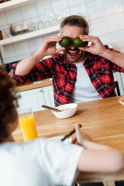 selective focus of father covering eyes with ripe avocados near curly boy  clipart