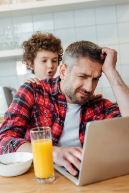selective focus of curly and noisy son touching tired freelancer father working from home clipart