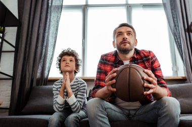 Odaklanmış çocuk ve baba basketbol oynarken şampiyonluğu izliyorlar. 