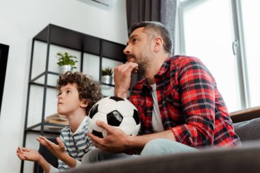 Sakallı babanın futbol oynayıp kıvırcık oğluyla şampiyonluk maçı izlediği seçici odaklanma.