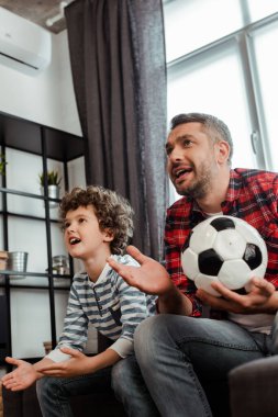 Duygusal ve sakallı baba futbol oynuyor ve kıvırcık oğluyla şampiyonluk maçı izliyor.