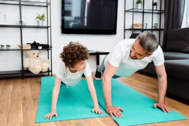 Yakışıklı baba ve kıvırcık oğul spor yapıyor, spor yapıyor ve birbirlerine bakıyorlar.