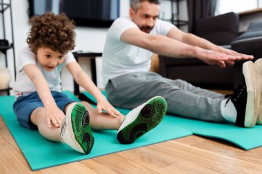 Kıvırcık oğlunun ve babanın fitness paspasları üzerinde egzersiz yapmasının seçici odağı 