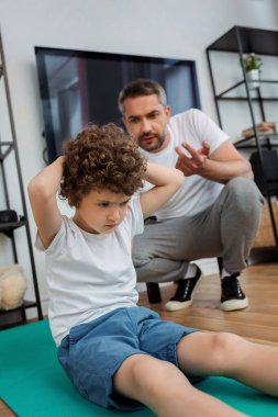 Kıvırcık çocuğun evde babalarının saydığı fitness paspası üzerinde çalışmasının seçici odağı.