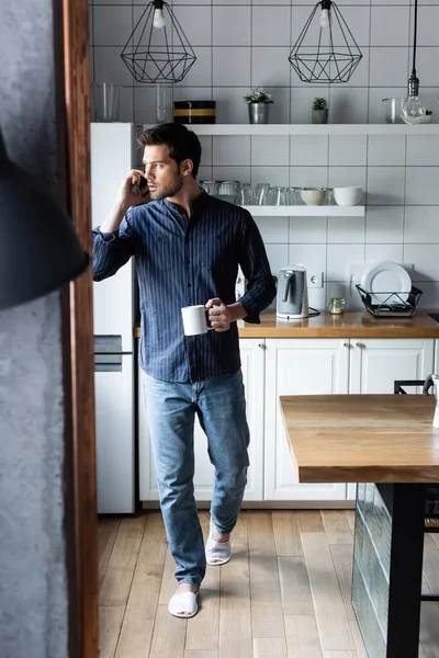 Homem Pensativo Segurando Xícara Café Enquanto Falava Celular Cozinha Durante — Fotografia de Stock