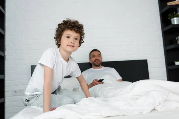 可爱的孩子坐在靠近父亲的床上拿着遥控器的选择性焦点 — 图库照片