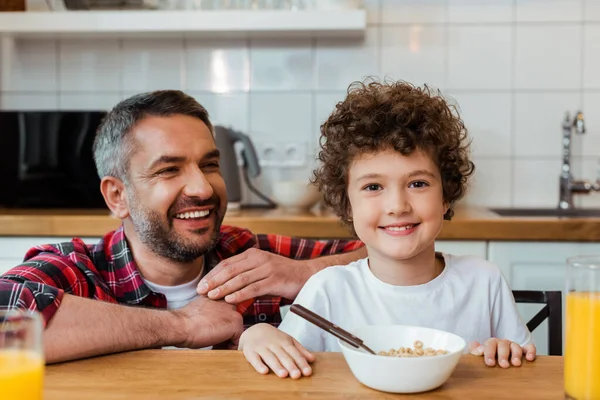 有选择地专注于快乐的父亲微笑着 卷曲着的儿子靠近早餐放在桌上 — 图库照片