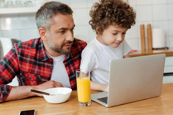 ハンサムな父親と中子は台所でノートパソコンを見て — ストック写真