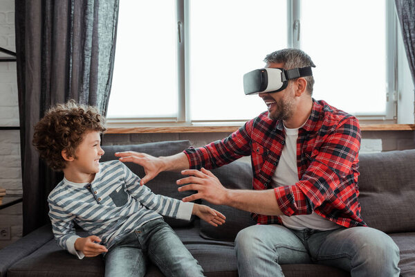 cheerful father in virtual reality headset gesturing near happy son