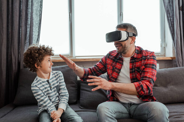 bearded father in virtual reality headset gesturing near happy son