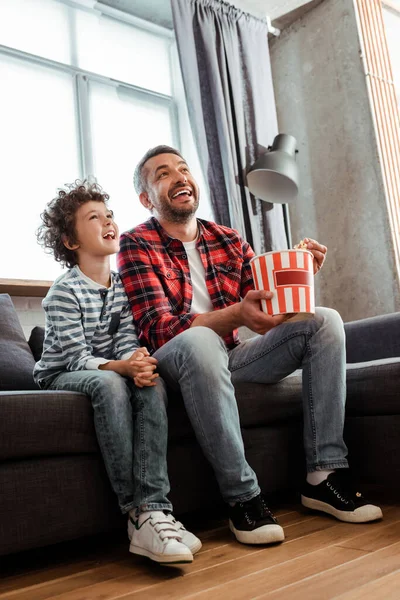 Garoto Feliz Encaracolado Assistindo Filme Perto Pai Segurando Balde Pipoca — Fotografia de Stock