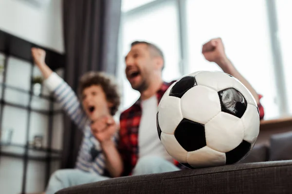 selective focus of football near cheerful father and son watching championship in living room 