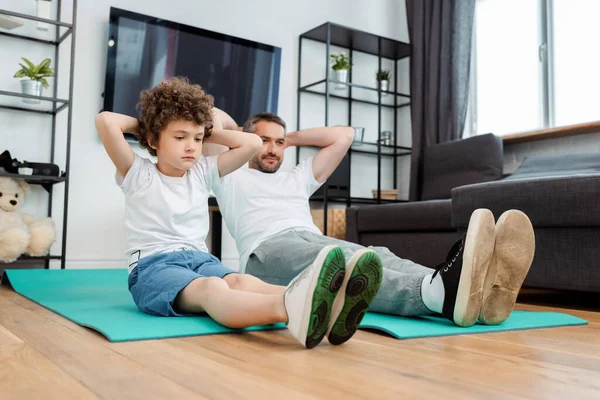 curly kid and bearded father working out on fitness mats at home