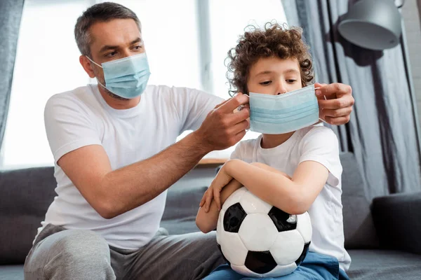 Padre Indossando Maschera Medica Sul Figlio Riccio Con Calcio — Foto Stock