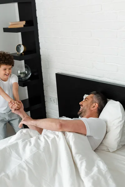 Niño Rizado Cogido Mano Mientras Juega Con Padre Feliz Dormitorio — Foto de Stock