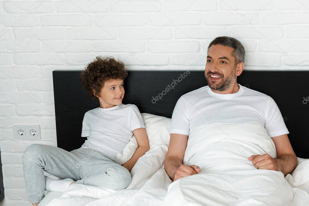 curly boy looking at bearded father in bedroom 