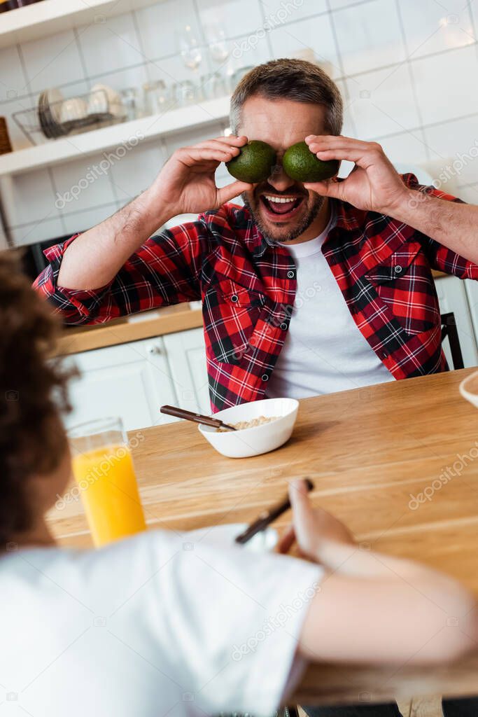 selective focus of father covering eyes with ripe avocados near curly boy 