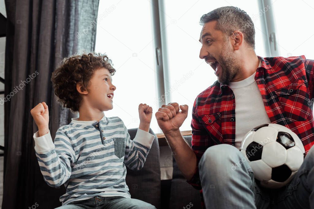 cheerful kid and happy father holding football while looking at each other