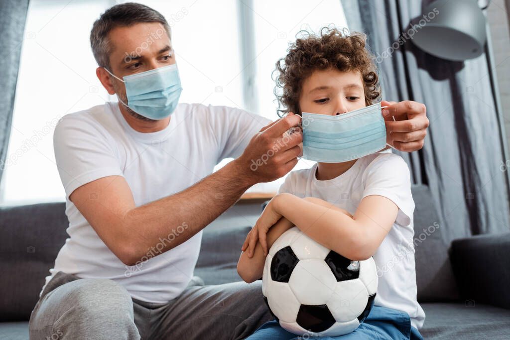 father wearing medical mask on curly son with football 