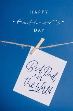 White greeting card with best dad in the world illustration hanging on rope with clothespins isolated on blue clipart