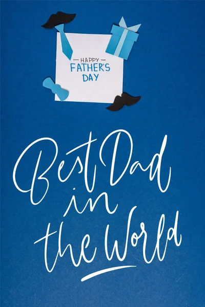 top view of greeting card with lettering happy fathers day and paper craft creative decorating elements on blue background, best dad in the world illustration