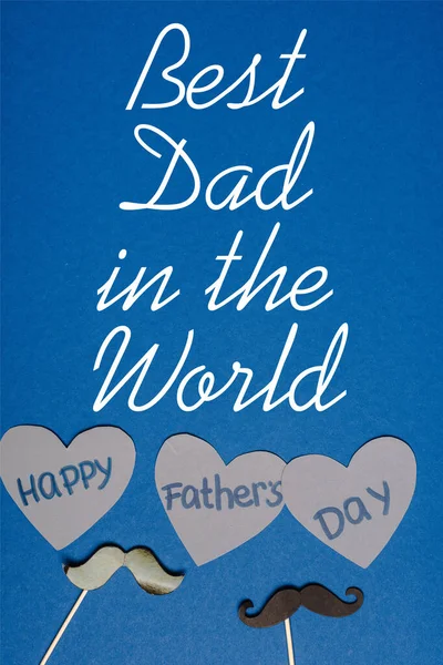 top view of decorative black mustache and paper cutted grey hearts with lettering happy fathers day on blue background, best dad in the world illustration