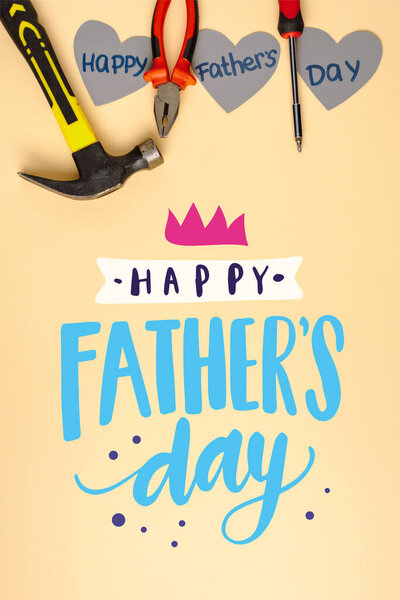 top view of hammer, screwdriver, pliers and grey paper hearts on beige background, happy fathers day illustration