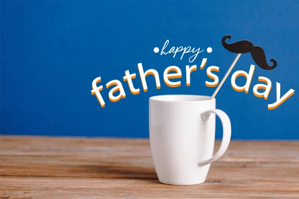 白いカップと黒い装飾紙青い幸せな父親の日のイラストに隔離された木製の表面に偽の口ひげ — ストック写真