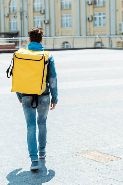 Back view of delivery man carrying thermo backpack on urban street 