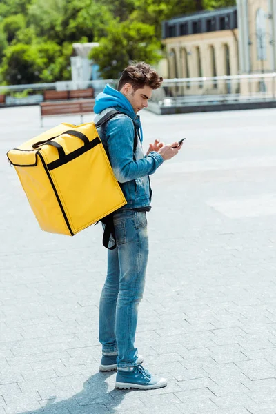 城市街道上使用智能手机携带背包的信使的侧视图 — 图库照片