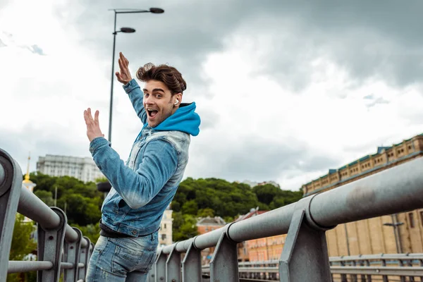 Side view of happy man in earphones looking at camera while walking on urban street