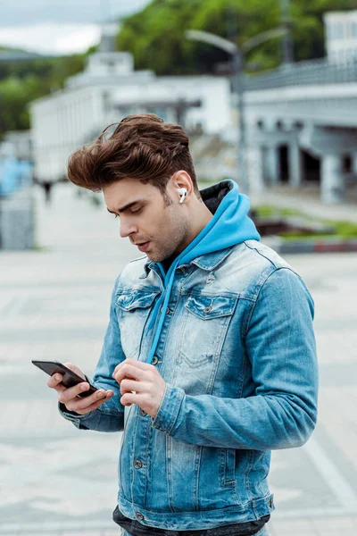 Young man in earphones using smartphone on urban street