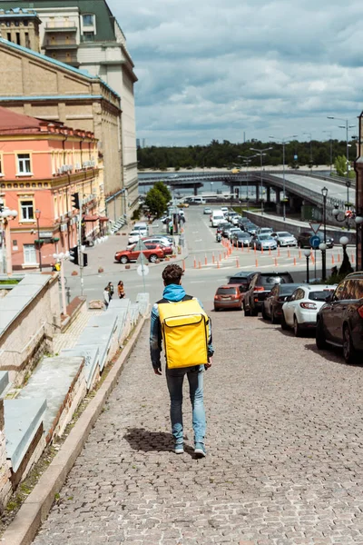 Back view of delivery man with thermo backpack walking on paving stone walkway on urban street — Stock Image Back View Delivery Man Thermo Backpack Walking Paving Stone Walkway Stock Picture