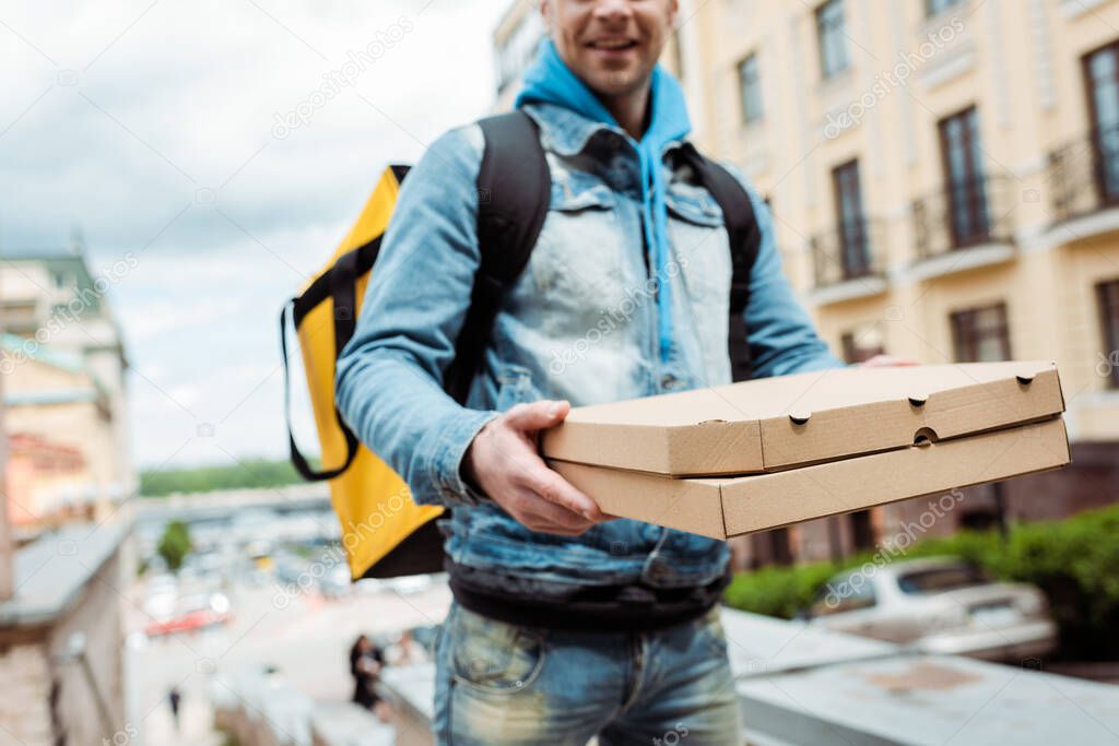 Cropped view of smiling delivery man holding cardboard pizza boxes on urban street 