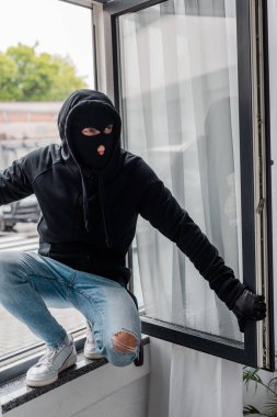 Kar maskeli bir soyguncu hırsızlık sırasında açık pencerede duruyor.