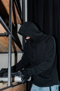 Soyguncunun maskeli ve deri eldivenli seçici odak noktası dolaptan kayıt çaları alıyor