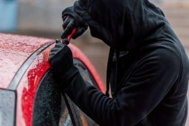 Araba kapısının camını açarken elinde tornavida tutan maskeli soyguncunun seçici odak noktası 