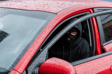 Kar maskeli soyguncunun açık kapılı arabada otururken kameraya baktığı seçici odak noktası 