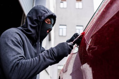 Selective focus of burglar using screwdriver while opening car door on urban street  clipart