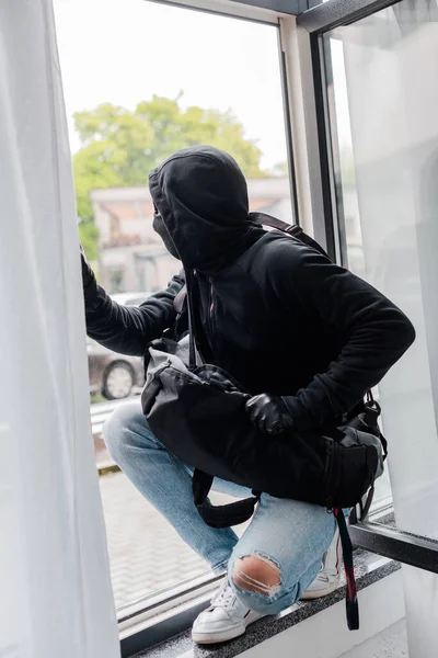 穿着巴拉克拉瓦和皮手套提包的强盗站在窗前的选择性焦点 — 图库照片