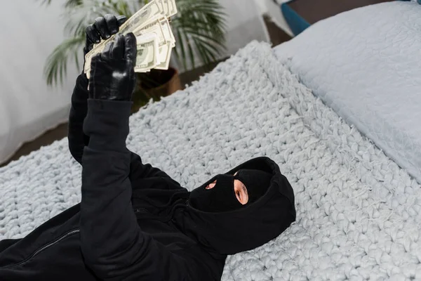 戴口罩和皮手套的小偷有选择地把焦点放在床上数钱钞票上 — 图库照片