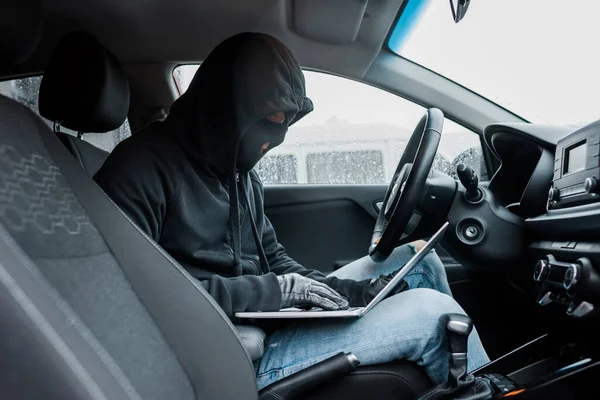 坐在车里时 穿着巴拉克拉瓦和皮手套的抢劫犯使用笔记本电脑的侧视图 — 图库照片